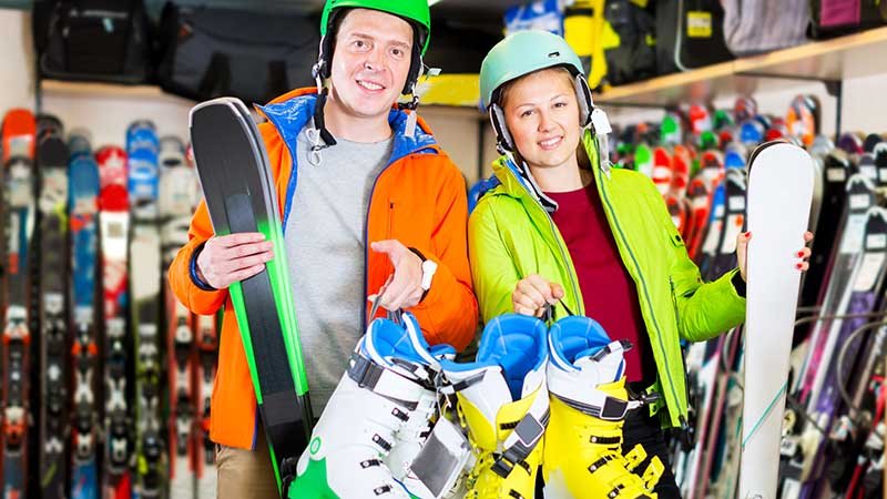 Mann og kvinne har på seg slalomutstyr og holder et par slalomski mens de står i et rom med slalomski langs veggene.