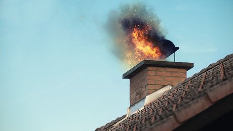 Flammer og røyk stiger opp fra en pipe på et hustak.