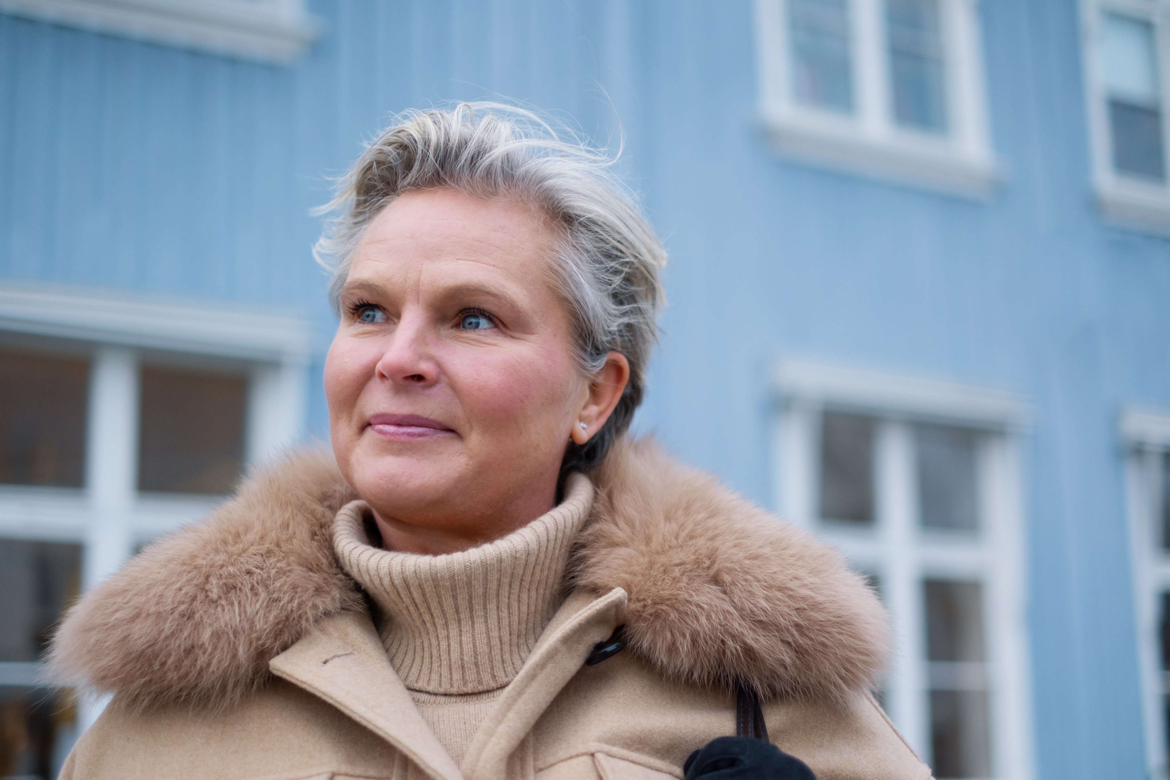 Kvinne som smiler foran et blått hus.