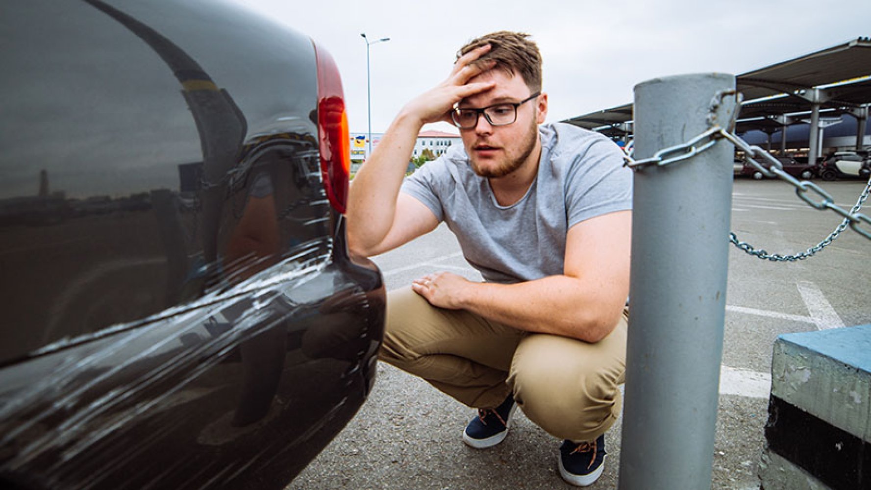 Ung mann holder seg til hodet og ser fortvilet på en oppskrapet bil. 