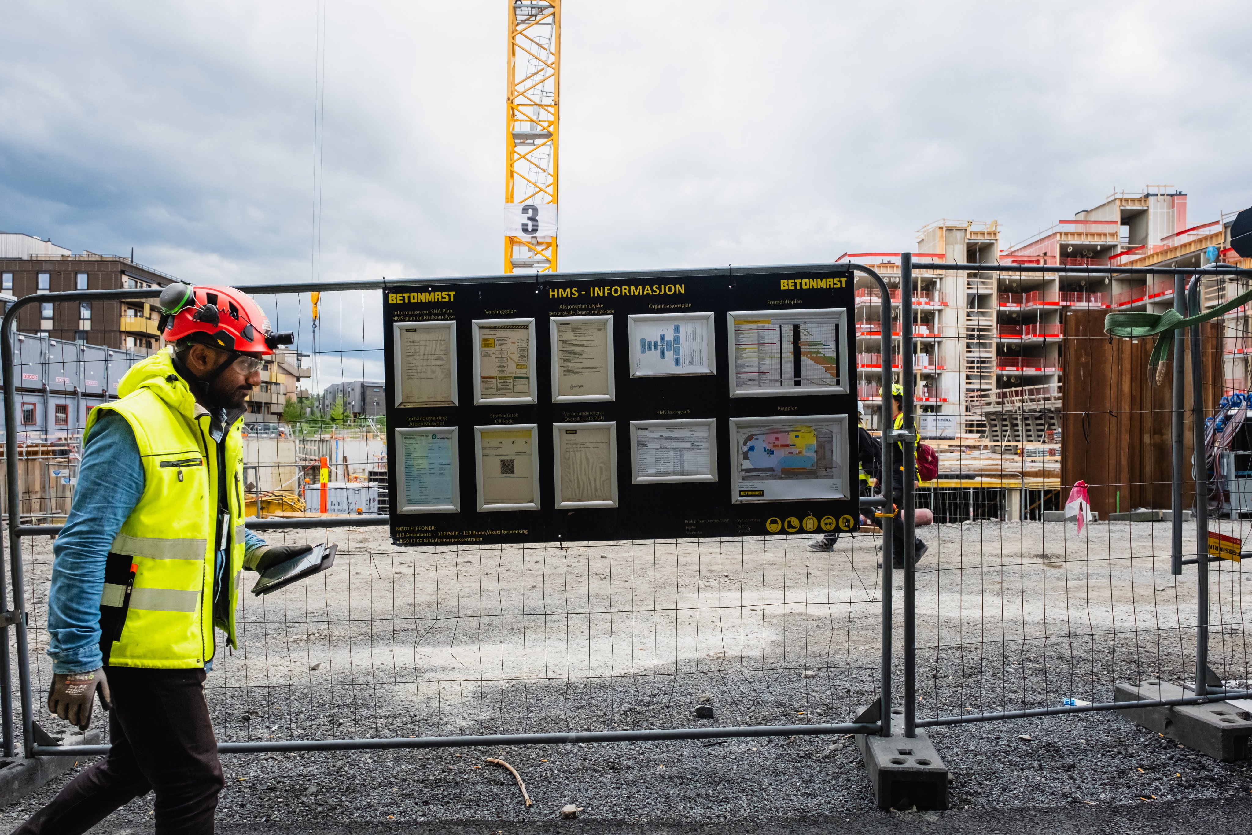 En anleggsarbeider som går forbi en tavle med informasjon om HMS på en byggeplass.