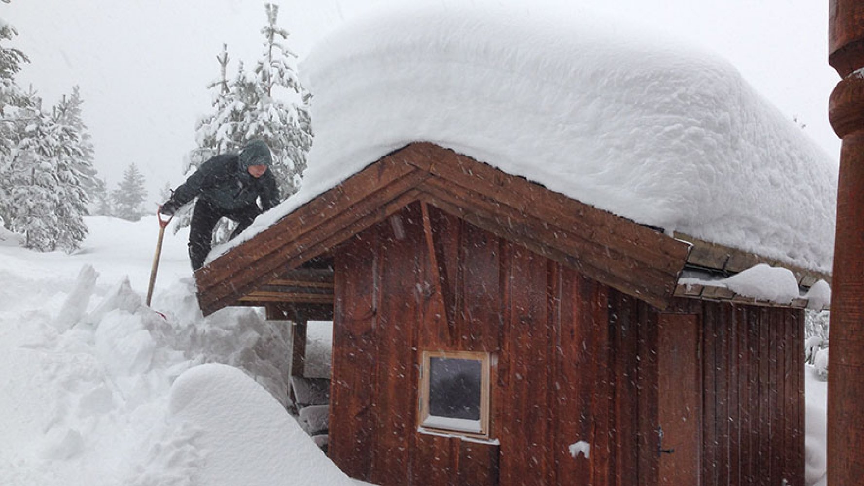 Det er vinter og en mann jobber med å skuffe hyttetaket for snø.