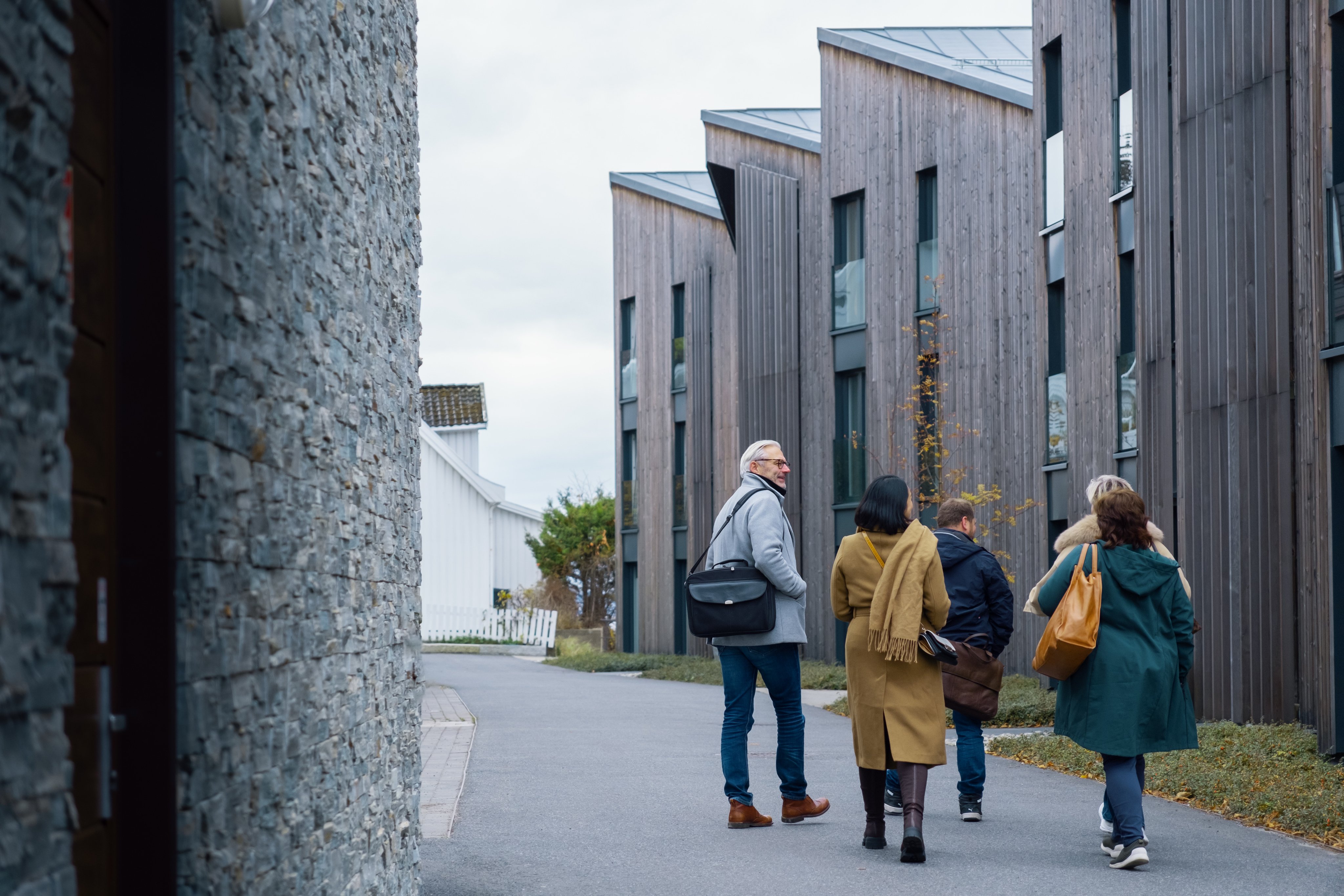Fem voksne går bortover en gangvei. Vi ser nybygg i bakgrunnen.