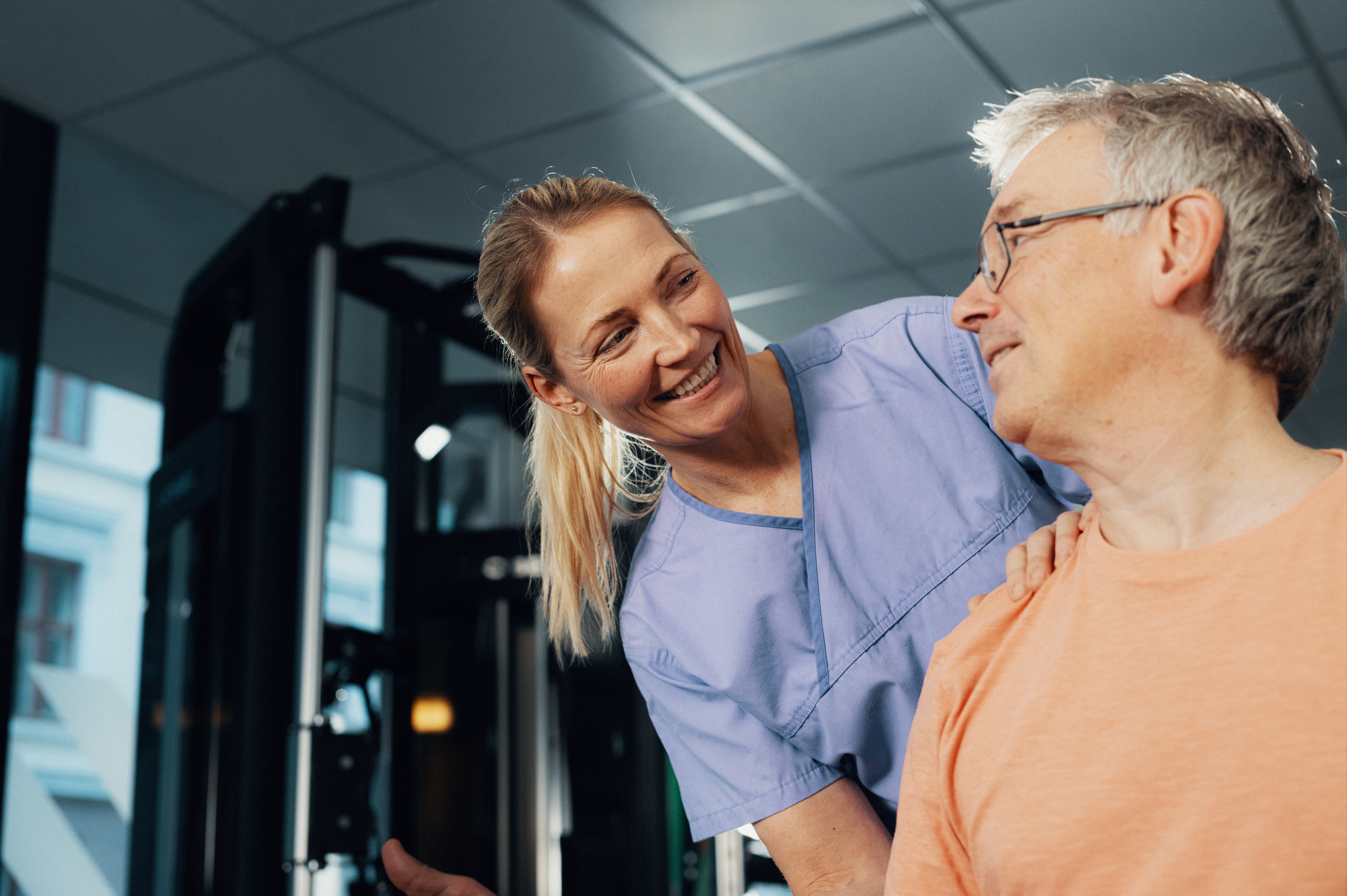 En fysioterapaut smiler til en pasient under behandling i et treningsrom.