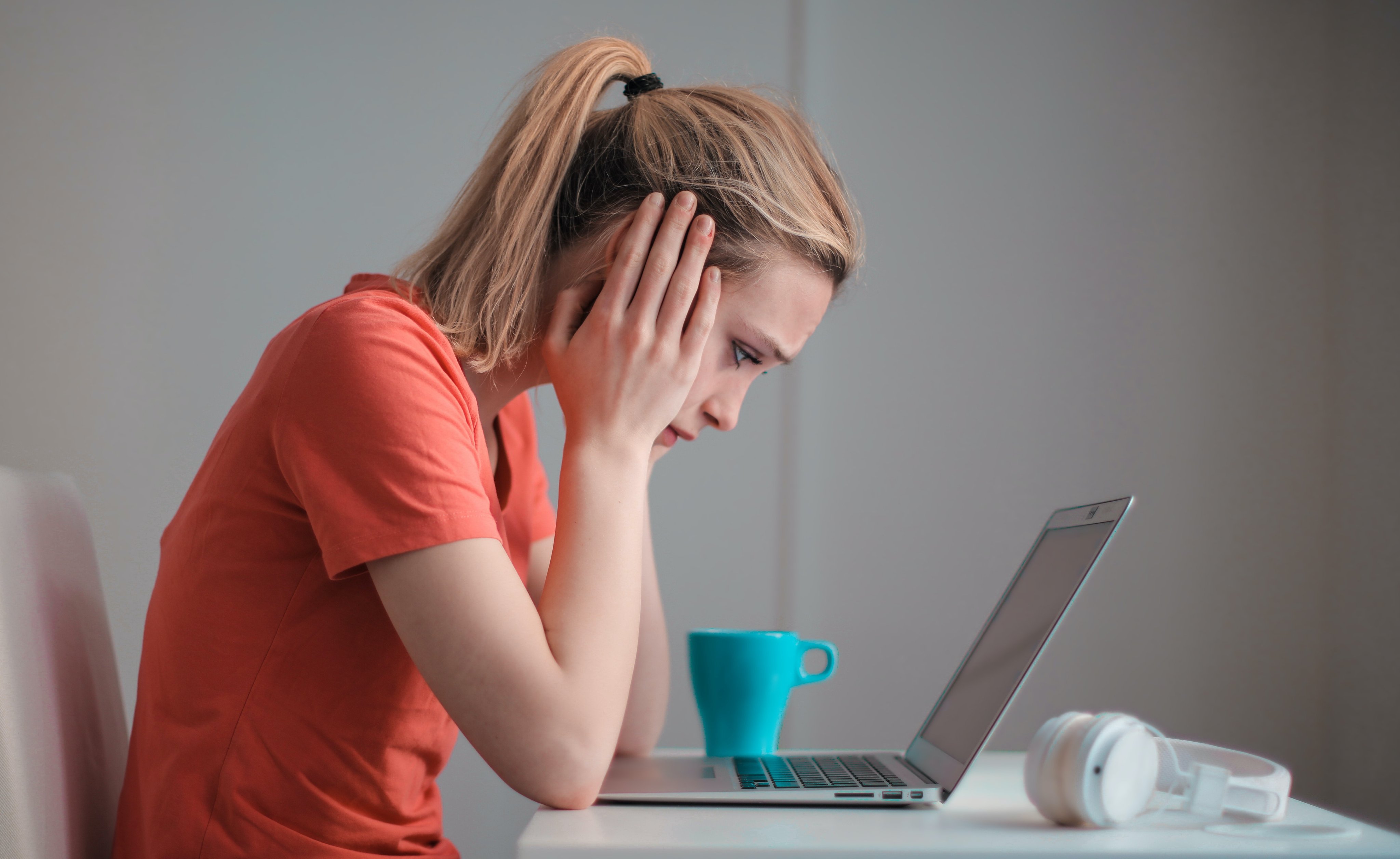 Ung dame ser på en laptop, holder seg til hodet og ser frustrert ut