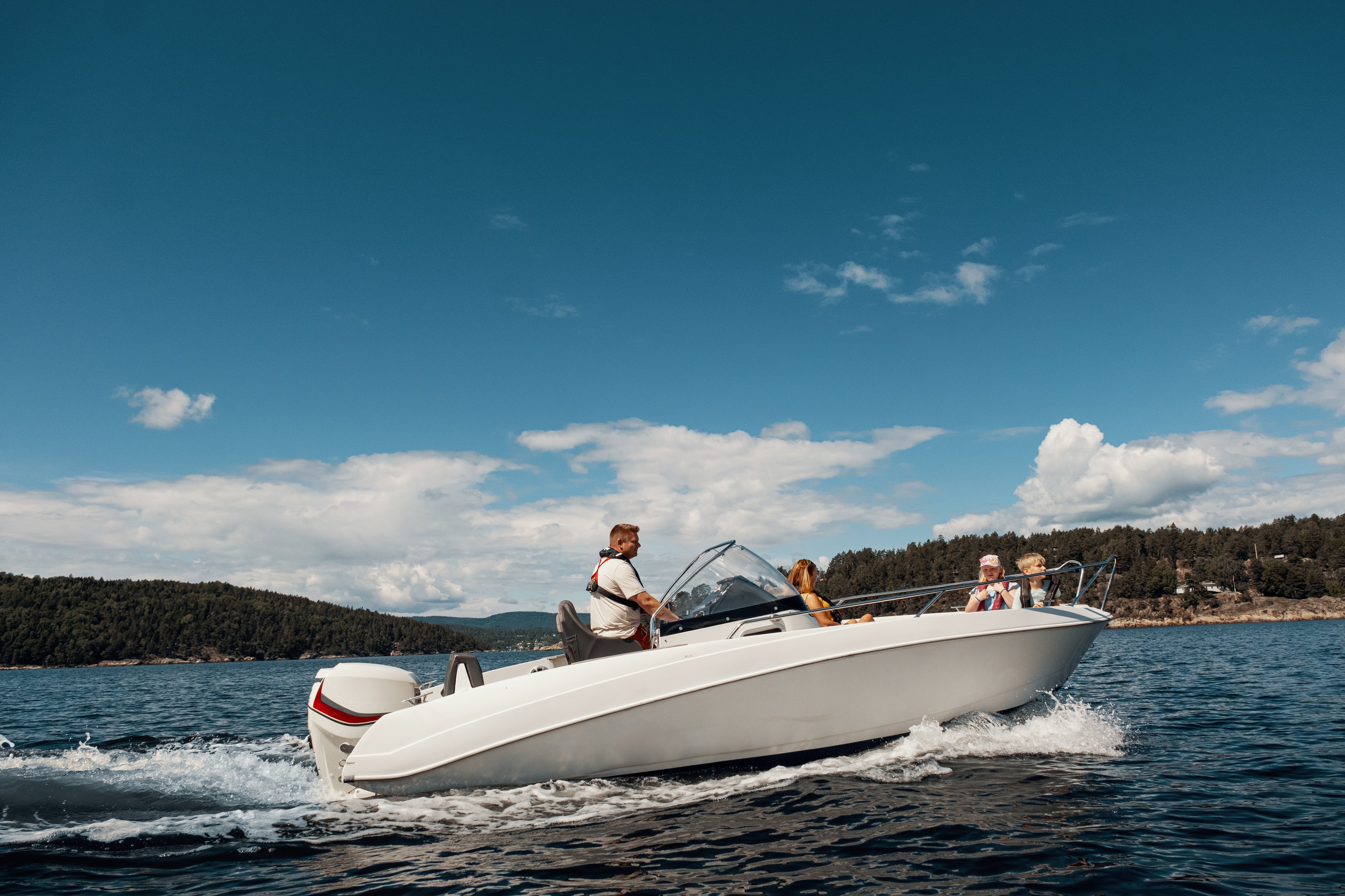 En familie sitter i en motorbåt ut på sjøen, en solfylt dag.