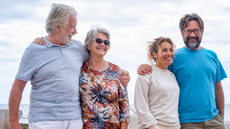 Et smilende eldre ektepar stående utendørs sammen med et smilende voksent ektepar
