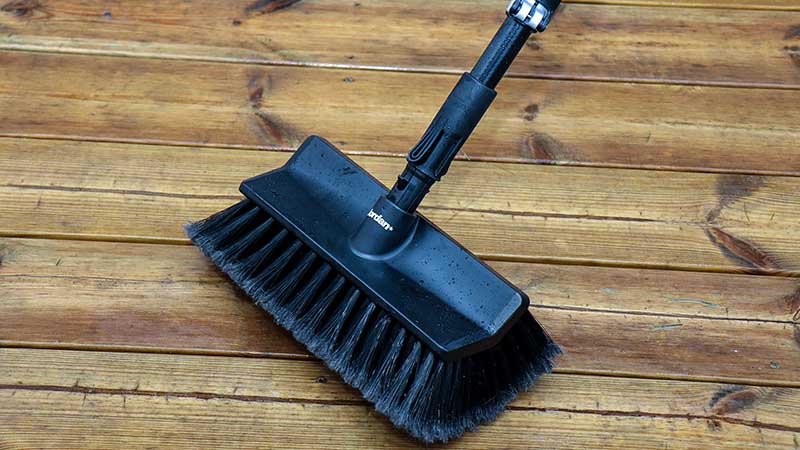 Svart vaskebørste med langt skaft på en våt treterrasse