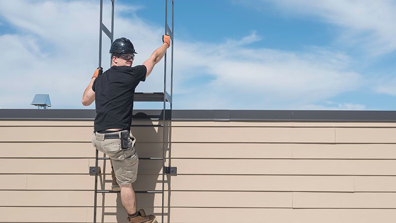 En mann bruker en stige til å klatre opp på et hustak.  