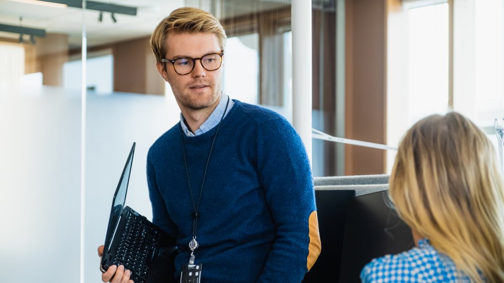 Mann står og snakker med en kollega i et kontorlandskap.