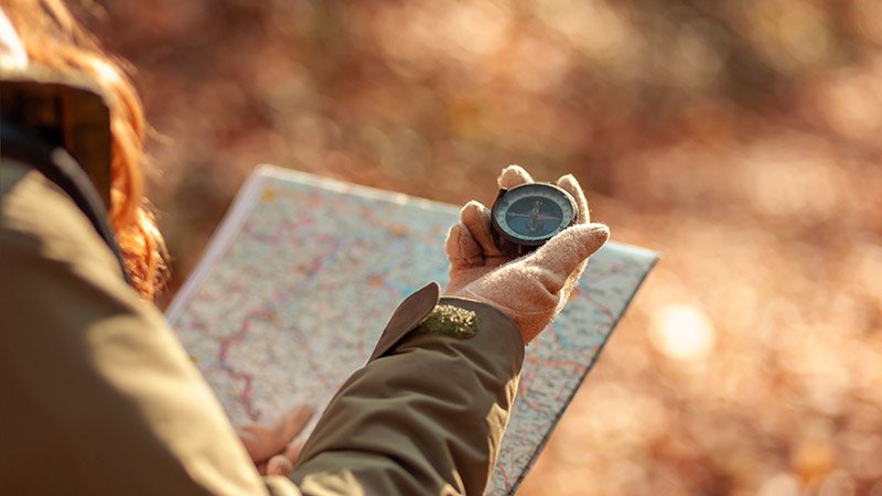 En kvinne holder et kart og en kompass i høstskogen.