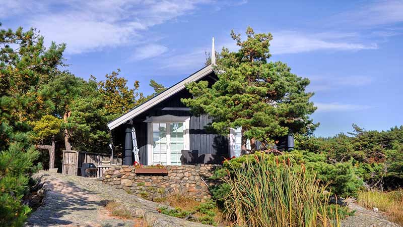 Liten hytte omgitt av trær og stein i et naturpreget område.