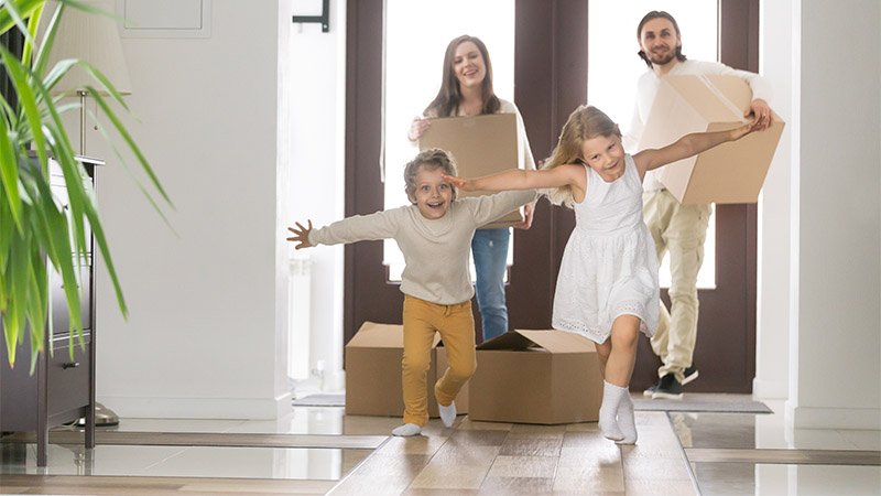 En mor, far og to små barn har nettopp kommet inn i det nye hjemme sitt og smiler.