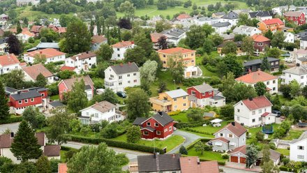 Oversiktsbilde av et boligområde med mange frittstående hus i ulike farger, omgitt av hager og trær.
