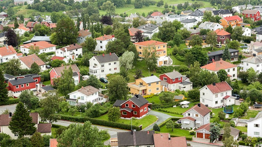 Oversiktsbilde av et boligområde med mange frittstående hus i ulike farger, omgitt av hager og trær.