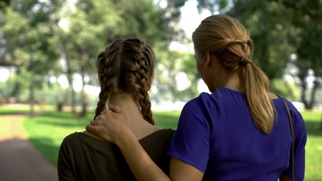 To kvinner står med ryggen til mens de ser utover en park. Den ene holder en hånd rundt den andre.