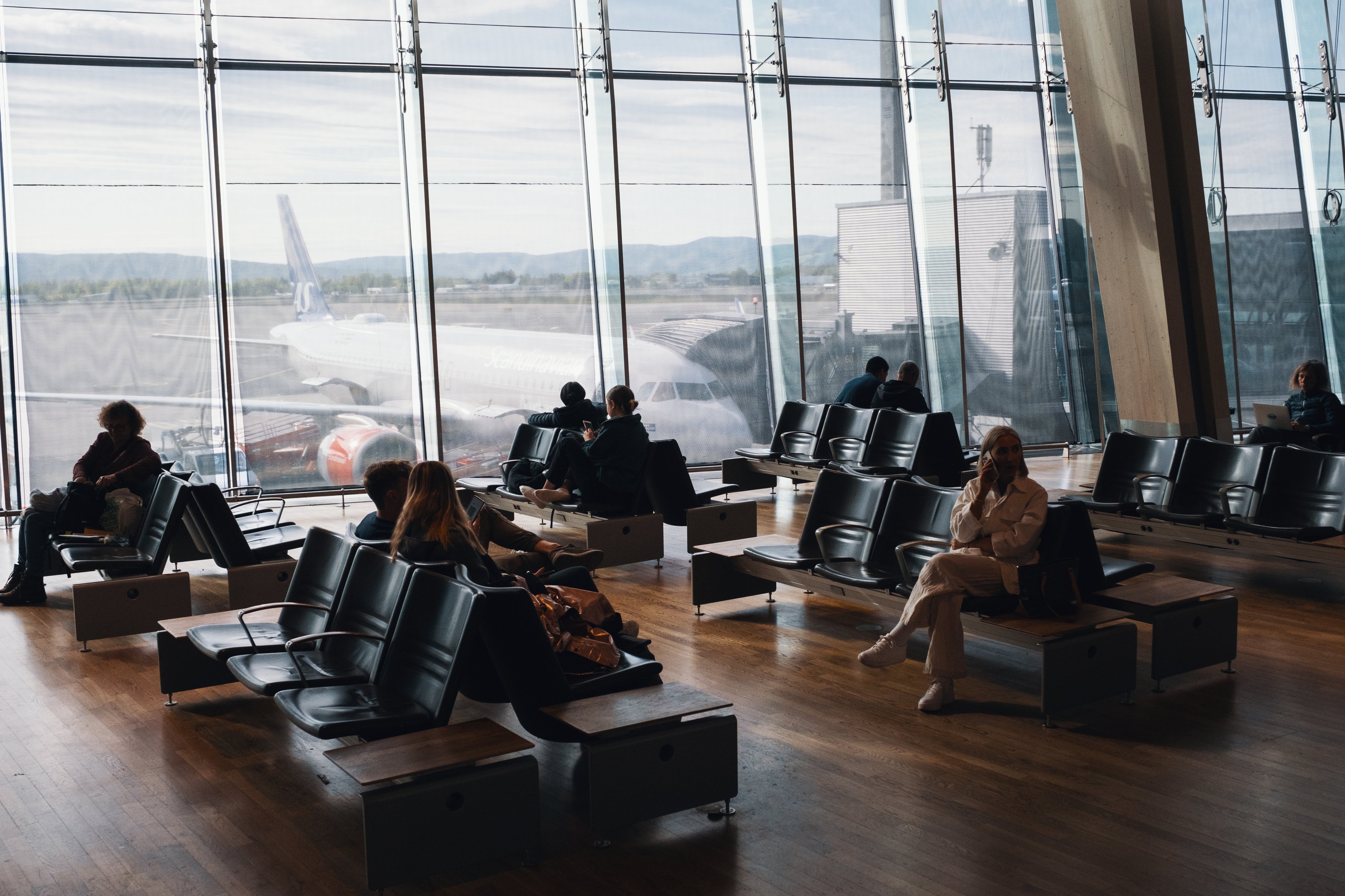 Passasjerer sitter ved gaten på en flyplass med utsikt mot et fly som er parkert.