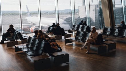 Passasjerer sitter ved gaten på en flyplass med utsikt mot et fly som er parkert.