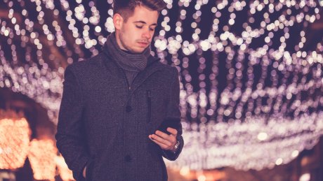 En ung mann står under gatejulelys mens han ser på telefonen.