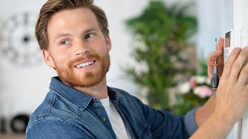 Mann holder en skrutrekker samtidig som han holder en ringeklokke mot ytterveggen. 