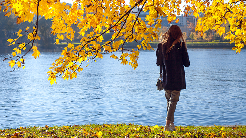 En dame som står under et tre og ser utover en elv.