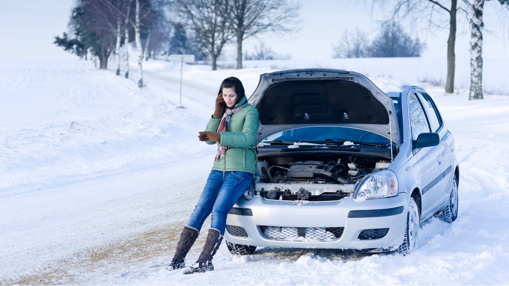 Bil med åpent panser står i snøen mens en person ringer etter hjelp.