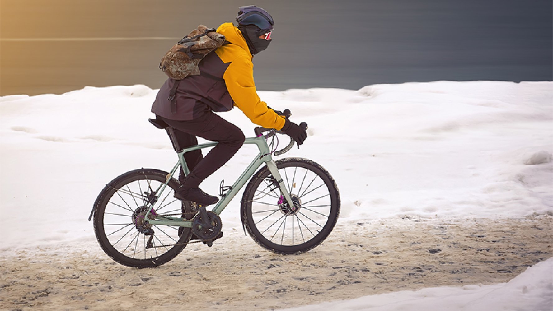 En mann sykler på en vintervei med snø, iført vinterklær og ryggsekk.