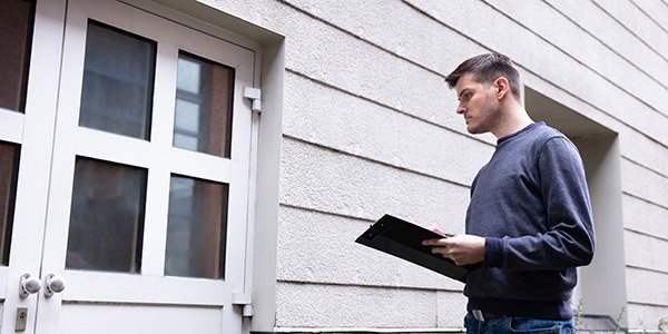 En mann står med en sjekkliste i hendene utenfor en bolig.