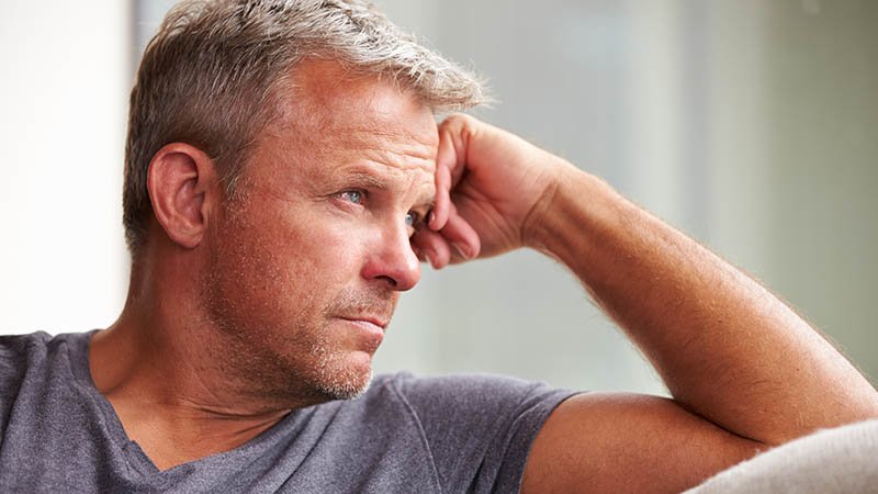 Mann med grått hår hviler hodet på hånden.