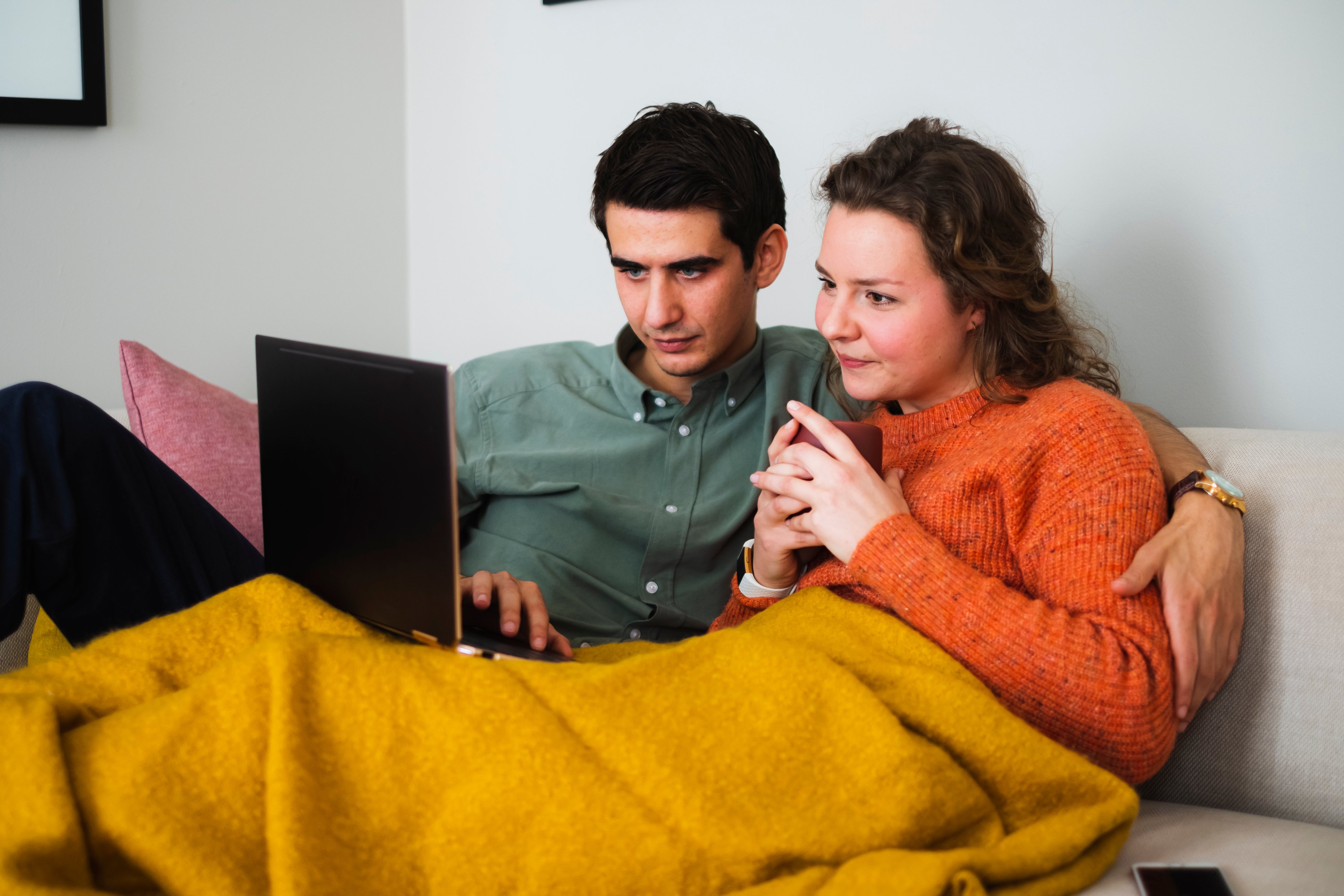 Ungt par sitter i sofaen og ser på en laptop de har i fanget.