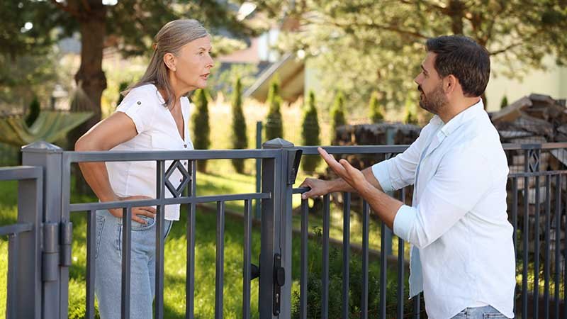 To naboer står og krangler over gjerdet en sommerdag