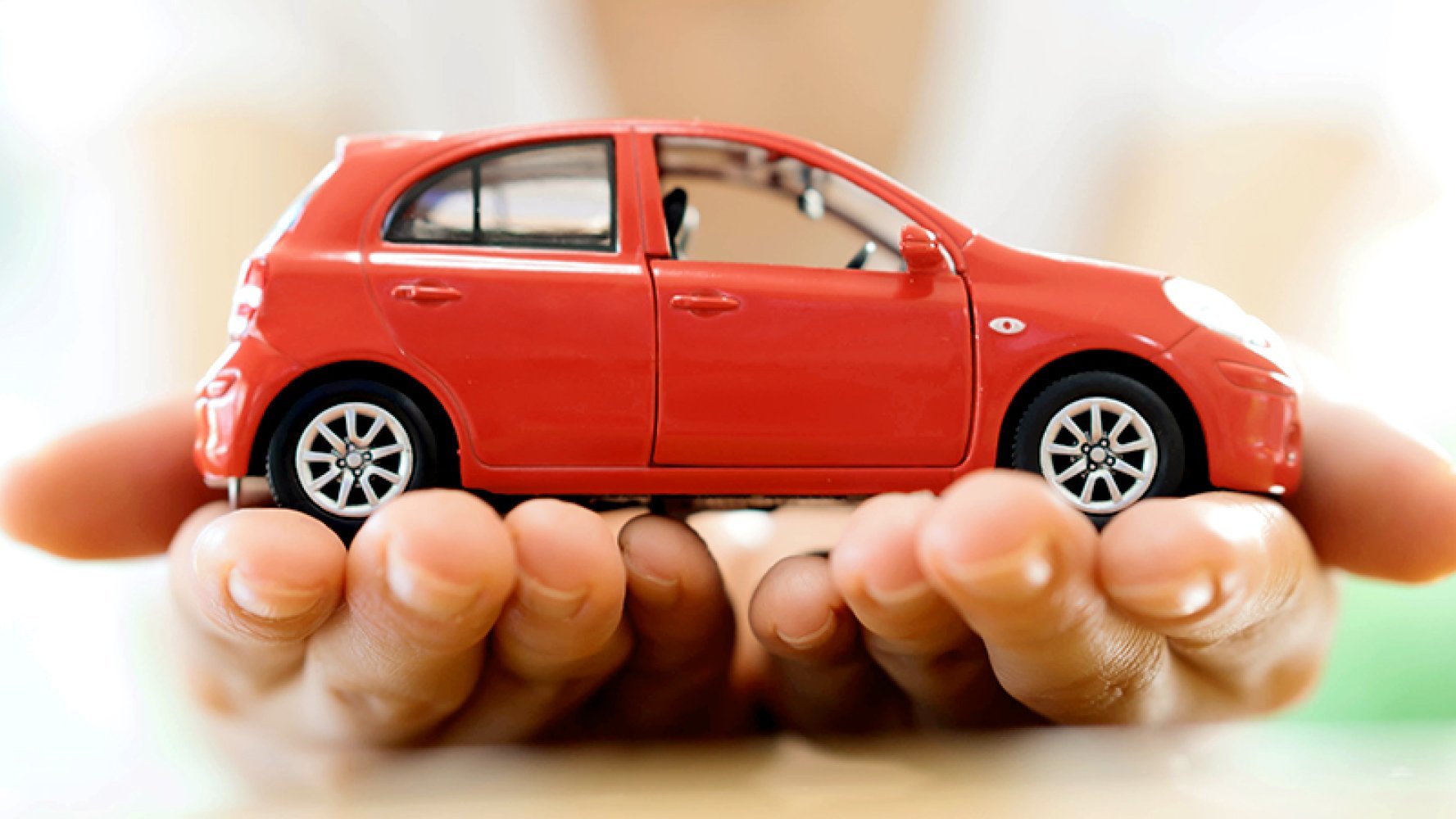 Nærbilde av to hender som har en liten bil på håndflatene.