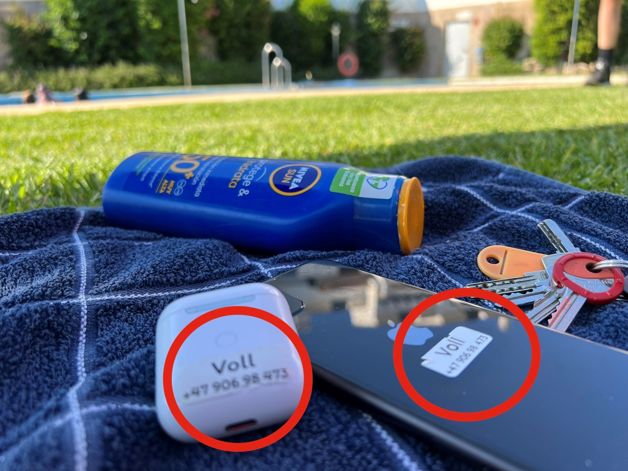 Nærbilde av lapp med navn og telefonnummer festet til en mobil og airpods.