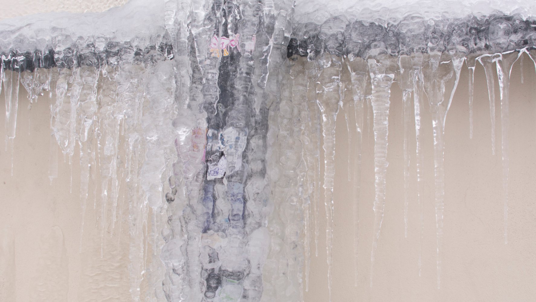 Frosset vannrør med tykke islag og istapper hengende ned fra en vegg.