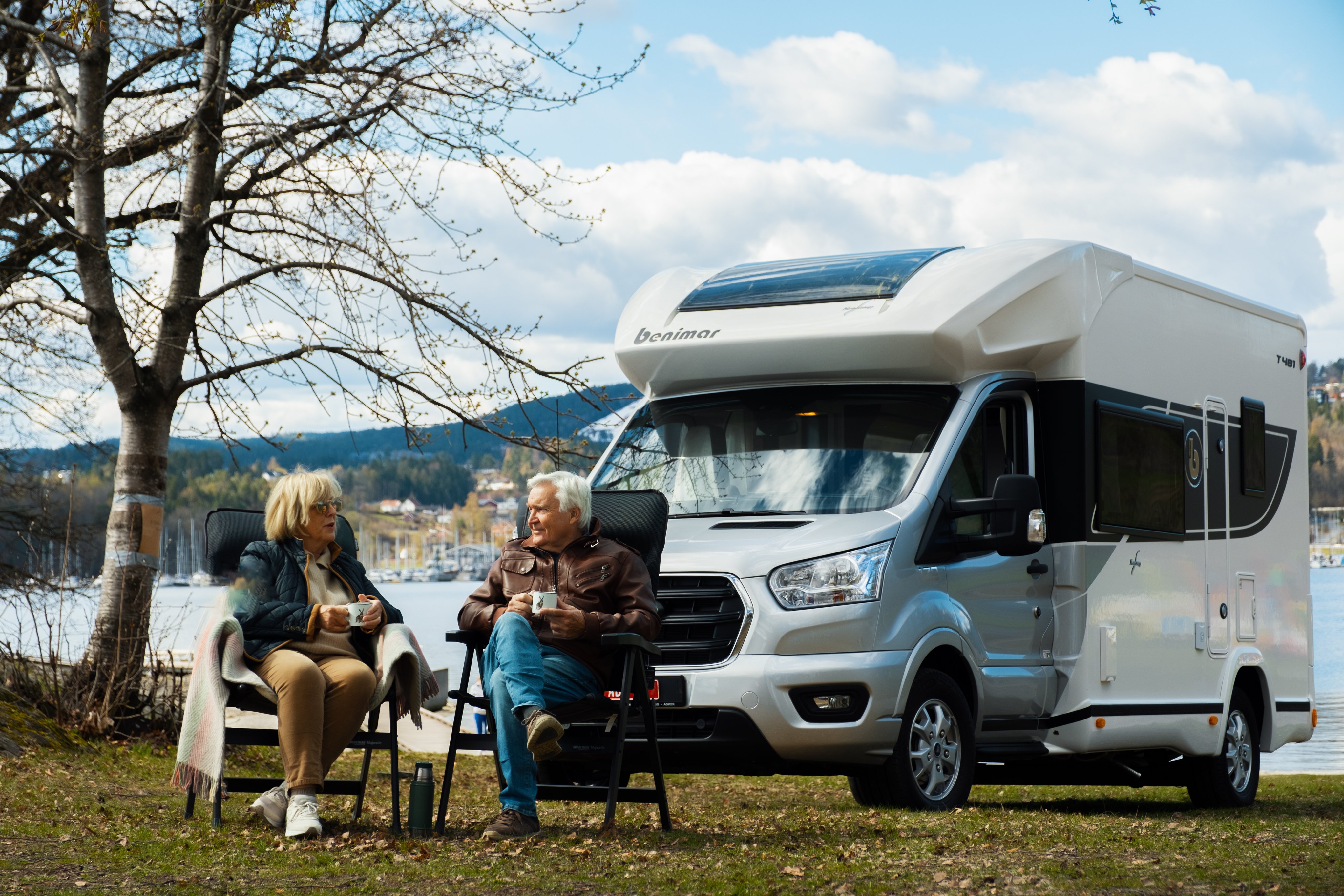 Et eldre ektepar sitter utenfor bobilen sin og nyter en kopp med kaffe.