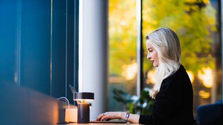 Kvinne ved skrivebord som jobber på datamaskin ved et vindu.