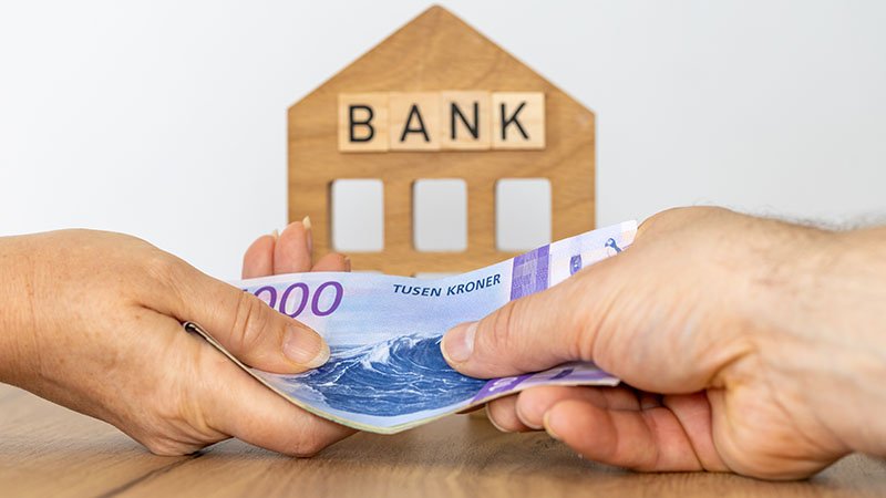 To hender utveksler norske tusenkronerssedler foran en trefigur formet som et hus med ordet BANK.