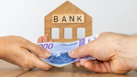 To hender utveksler norske tusenkronerssedler foran en trefigur formet som et hus med ordet BANK.