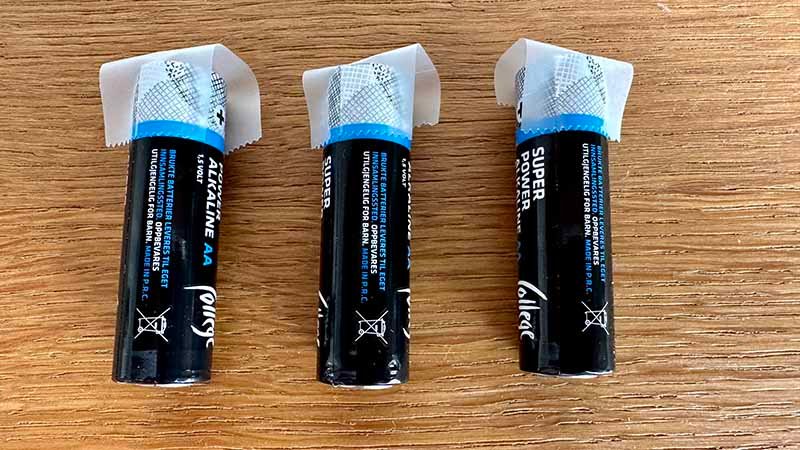 Tre små AA-batterier ligger på et bord og har teip på batteripolene.