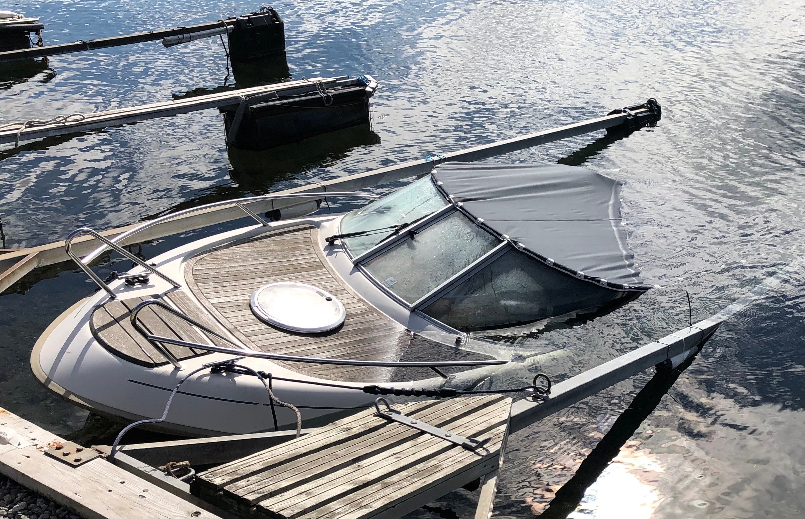 Motorbåt ligger delvis sunket ved en brygge, med baugen fortsatt over vann.