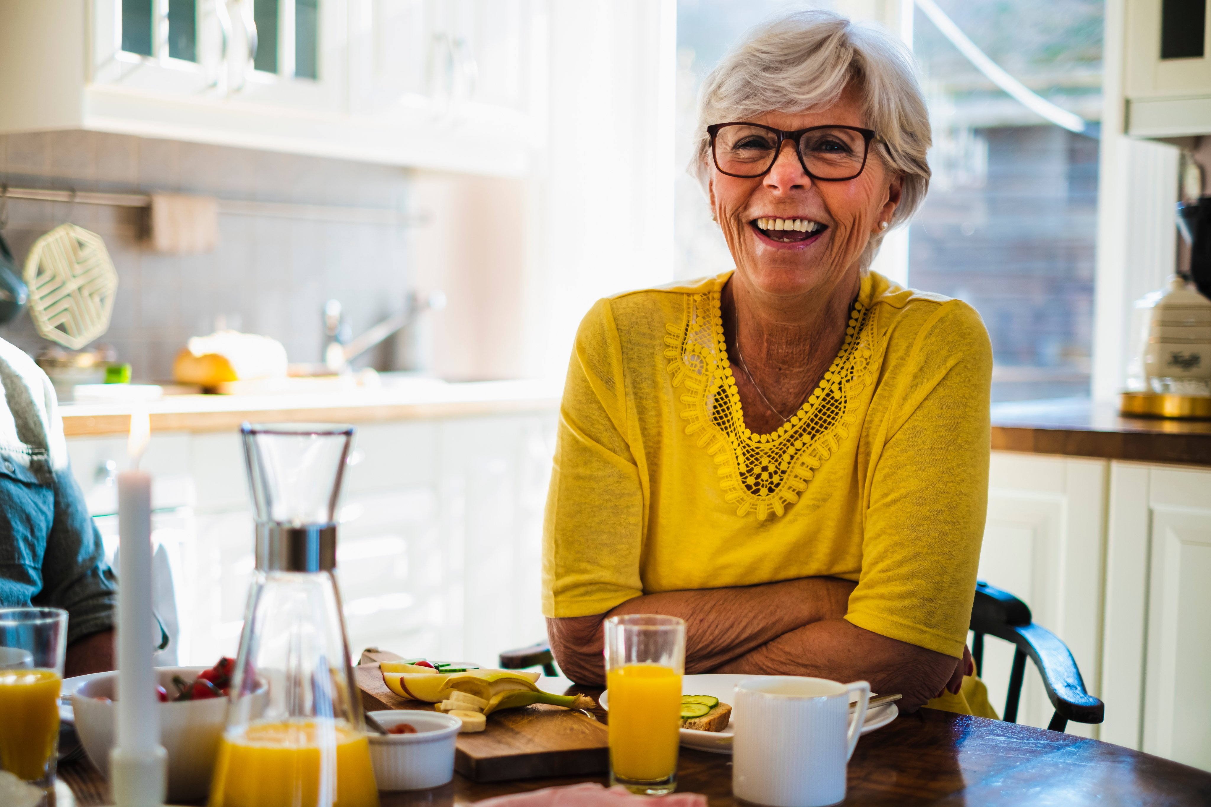 Kvinne sitter ved et kjøkkenbord og smiler.