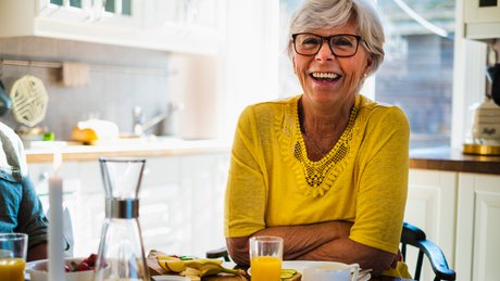 Kvinne sitter ved et kjøkkenbord og smiler.