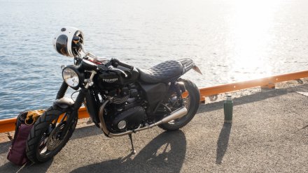 Motorsykkel parkert ved vannkanten med hjelm og bagasje.