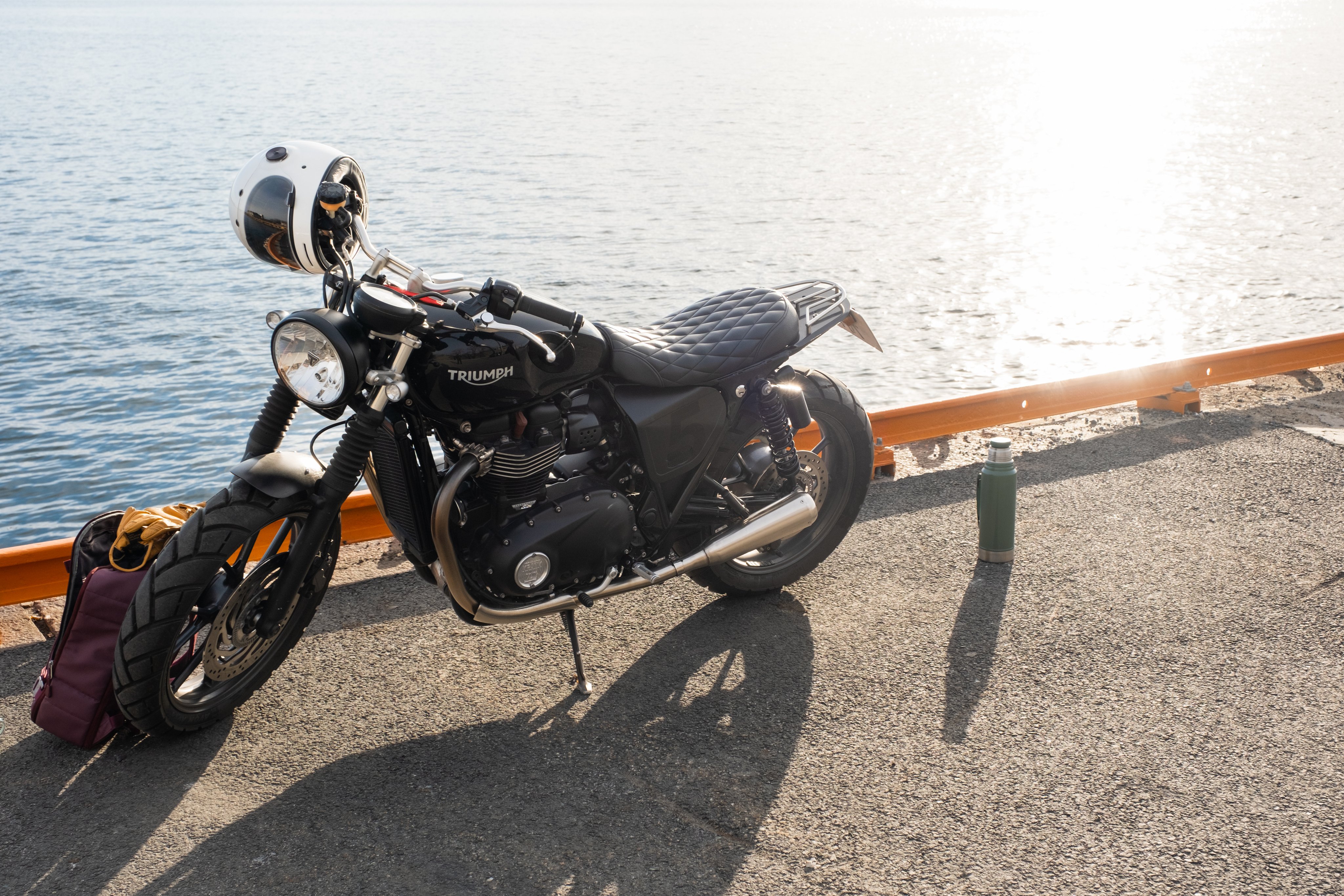 Motorsykkel parkert ved vannkanten med hjelm og bagasje.