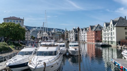 Havn med flere store båter og yachter, omgitt av fargerike bygninger og fjell i bakgrunnen.