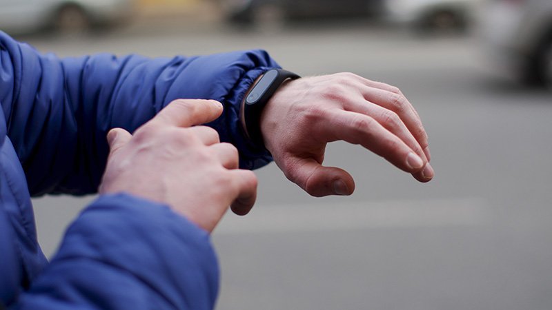 Person i blå boblejakke med en smartklokke på venstre arm holder armene opp for å se på klokka, med høyre arm pekende på klokka.