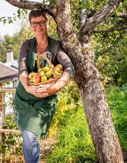 Marianne Utengen står under et epletre og holder rundt en kurv full av epler.
