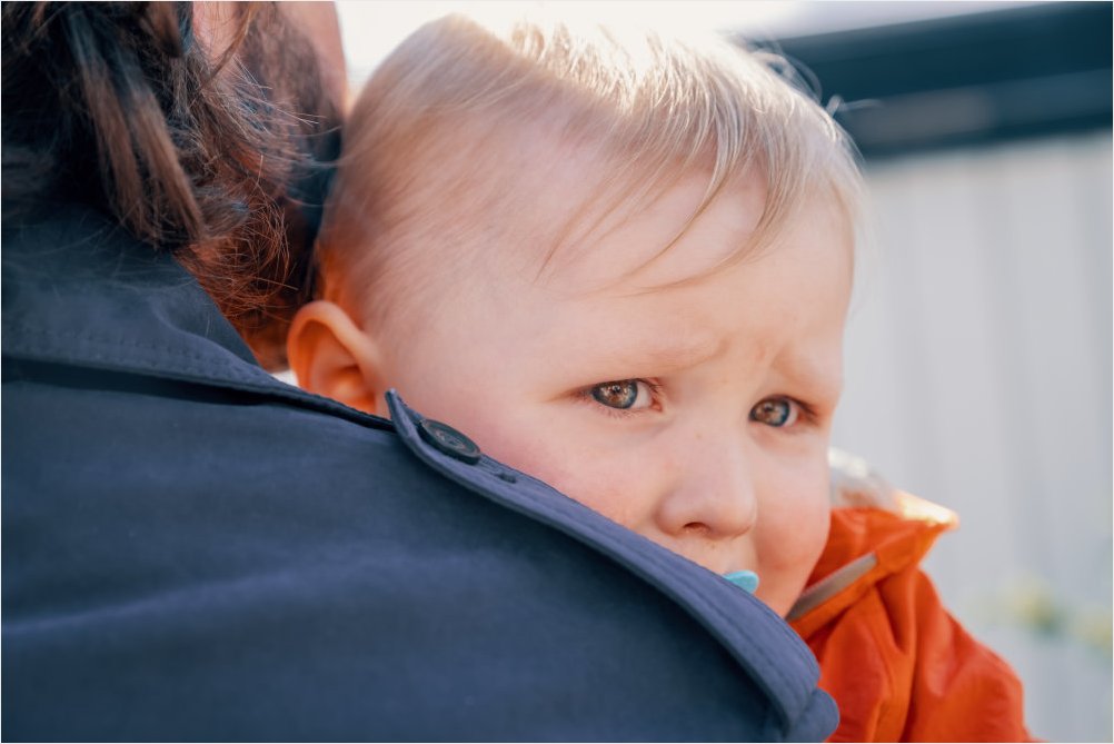 Nærbilde av et fortvilt barn som holdes og ser over skulderen på en voksen