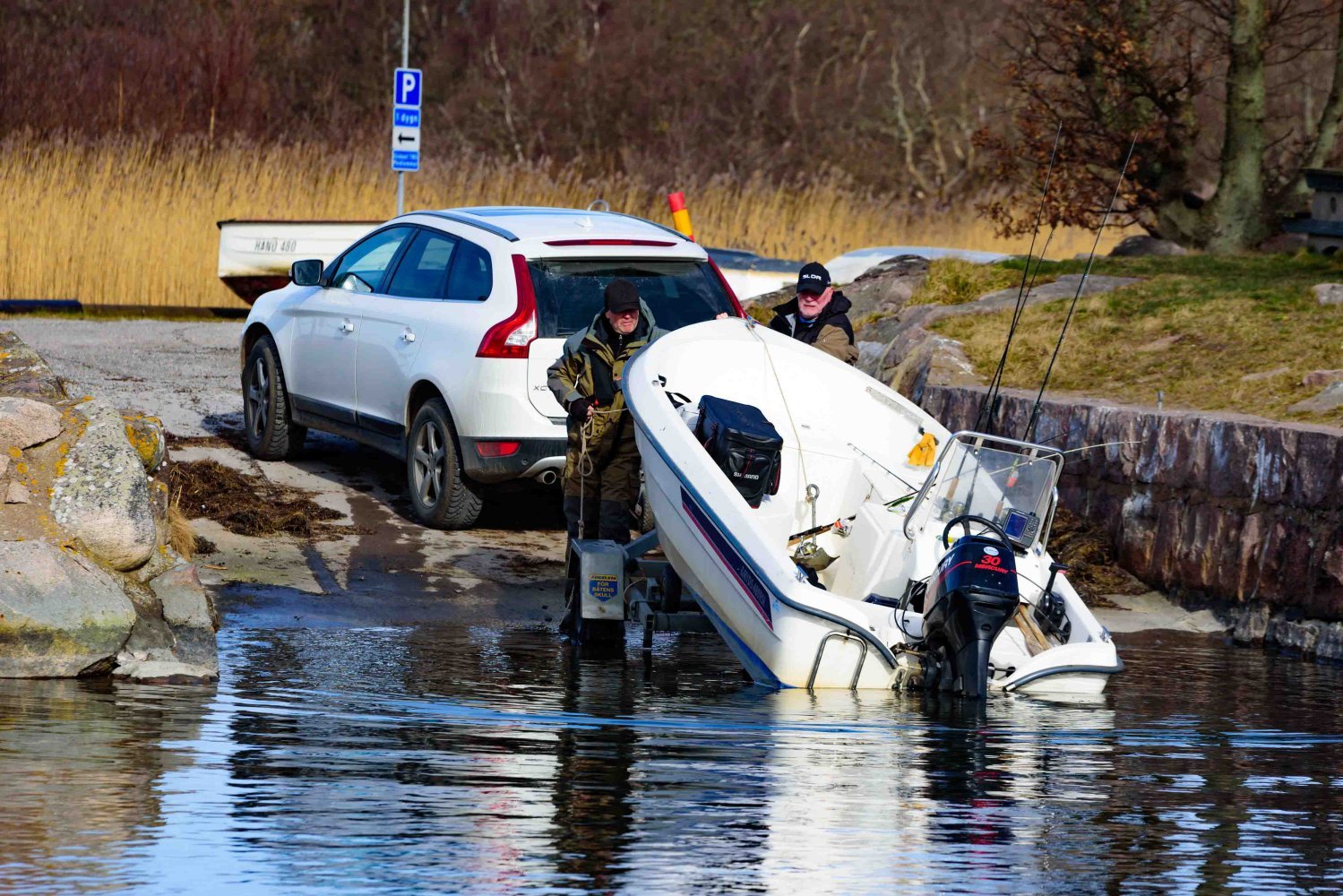 En bil står ved en båtrampe mens en liten motorbåt blir sjøsatt i vannet.
