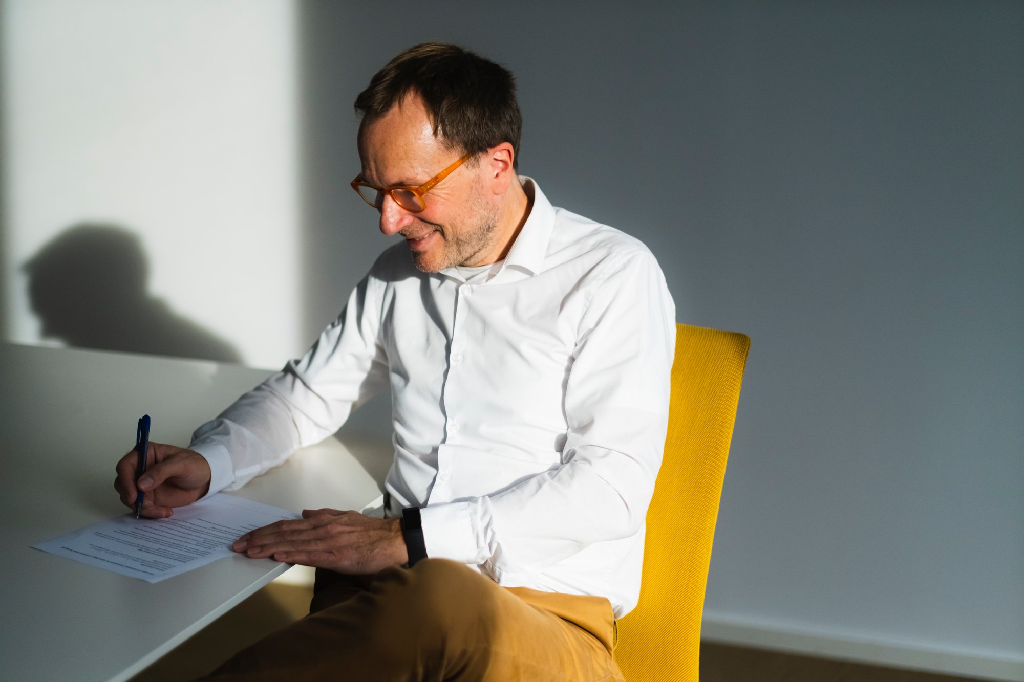 Mann med briller sitter og skriver med penn på pair.